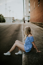a young woman sitting on a curb 