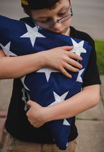 child carrying a folded flag and wearing a military cap 