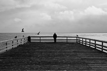 man looking at the ocean from a pier 