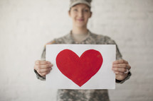 Red heart on white paper being held by an army soldier.