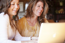 Mother and daughter laughing while working at a laptop computer.