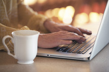 Hands typing on a laptop computer next to a coffee cup.