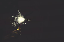 hand holding a sparkler and an American Flag background