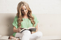 blonde woman sitting on a white couch reading a Bible