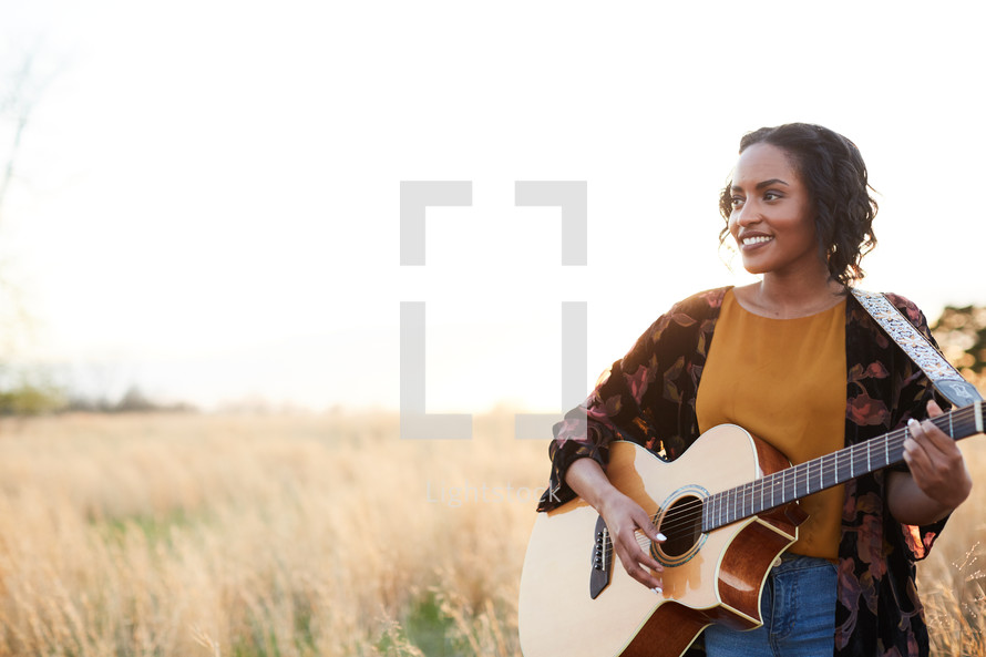 a woman standing in a field with a guitar 