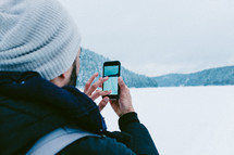 a man standing in snow taking pictures with his cellphone 