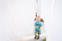 a toddler walking under hanging sheets 