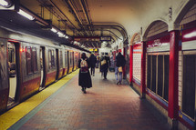 People walking through subway station next to a train