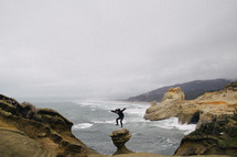 A man jumps in the air on cliffs by the ocean.