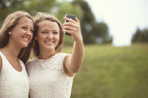 two girls taking a selfie with a cell phone.