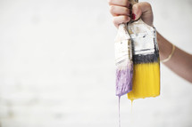 A woman holds two dripping paint brushes.