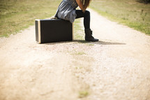 woman sitting on a suitcase on a dirt road 