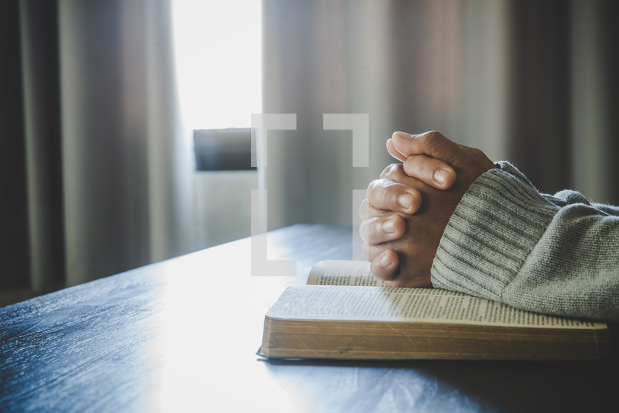 Asian woman praying to God with Bible open on a wooden table