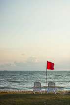 red flag by lawn chairs on a beach 
