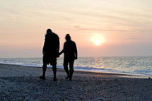 silhouette of a couple walking holding hands on the beach