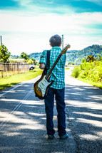 a child standing on a road with a guitar on his back 