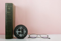 Bible spine, clock, and reading glasses 