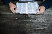 hands of a man reading a Bible at a picnic table 