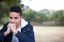 teen boy smiling with praying hands outdoors 