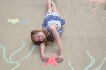 A little girl in a swim suit grabbing a starfish on an ocean scene painted on sidewalk chalk 