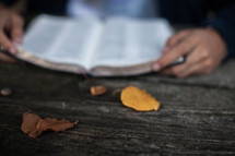 hands of a man reading a Bible at a picnic table 