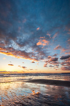 clouds over wet sand on a shore at sunset 