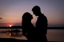 silhouette of a couple in love standing by a lake at dusk 