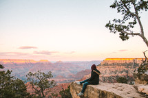 a man sitting at the edge of a cliff looking out at canyons 