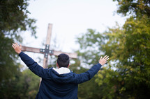 teen boy standing with raised hands in front of a wood cross