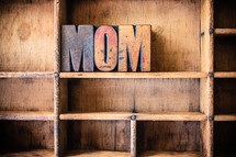 Wooden letters spelling "mom" on a wooden bookshelf.