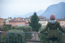 a woman standing at a railing looking out at a view of a European village 