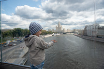 toddler boy standing in front of a river on a bridge 