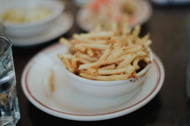 A bowl full of french fries on a dinner plate.