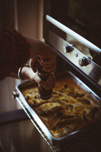 a woman putting pepper on a dish going into an oven 