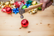 Hand holding a hammer, smashing a glass Christmas ornament on a wood board.