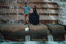 a couple holding hands walking along a fountain 
