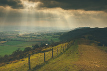 rays of sunlight from clouds above a green landscape 