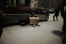 A homeless person sitting with a cardboard sign.