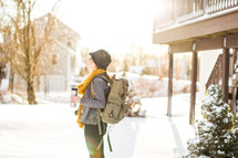 woman standing in the snow holding a coffee mug and wearing a backpack