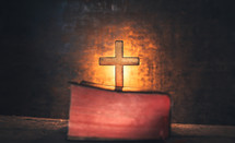 glowing cross behind a Bible 