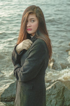 young woman standing on a shore looking back at the camera 
