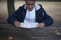 teen boy reading a Bible outdoors 
