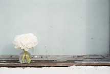 A vase of white flowers on an aged wooden board.