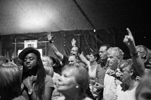 A diverse group of people standing and worshipping together in a large tent.
