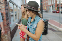 a young woman texting standing on a sidewalk with friends texting 