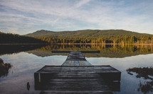 A wooden pier on a placid lake in the wilderness.