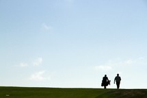 Silhouettes of two men walking along a golf course.