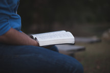 Holding an open Bible outside.
