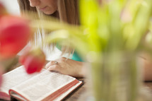 Woman reading the Bible on a wood table with tulips.