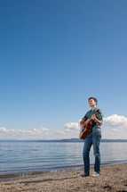 man playing a guitar outdoors by a lake